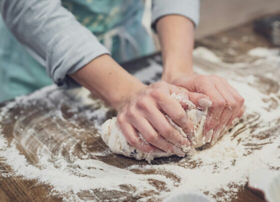 Person kneading dough on a floured wooden work surface.
