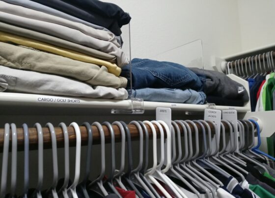 Folded clothing arranged on a closet shelf with clear dividers.