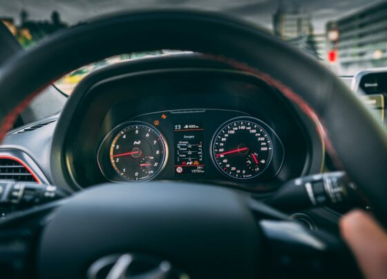 Driver's hands on a steering wheel in front of dashboard gauges