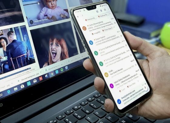 Person holding a phone displaying email beside an open laptop.