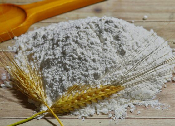 Mound of flour with wheat stalks and a rolling pin on a wooden surface.