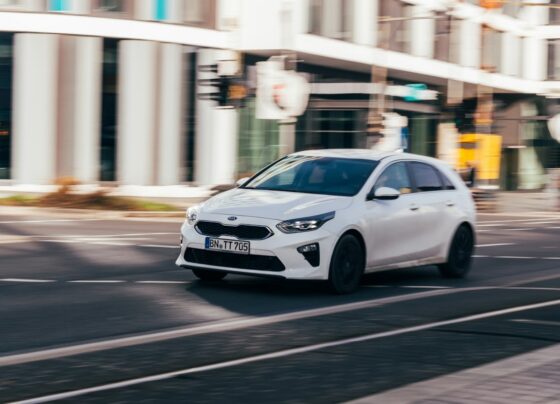 White Kia hatchback traveling on a street