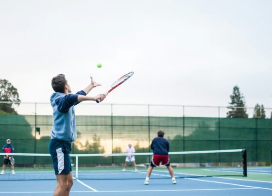 Tennis players on an outdoor doubles court, with the nearest player preparing to serve.