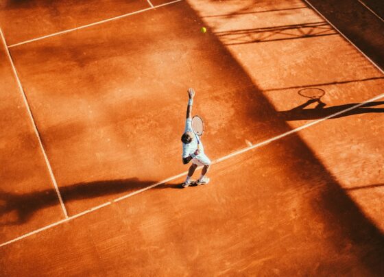 Overhead view of a tennis player serving on an orange clay court.